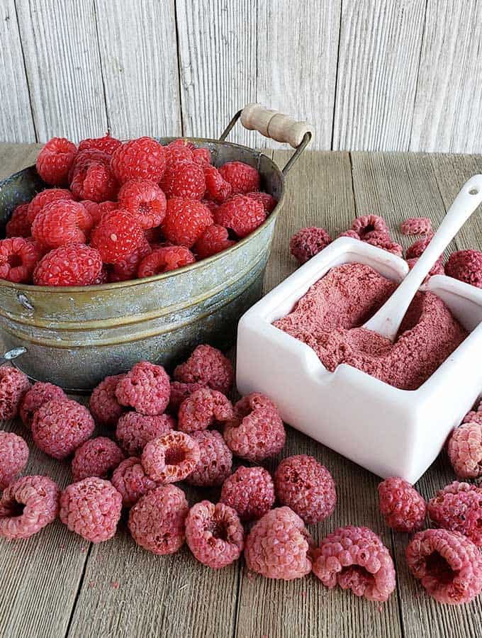 Fresh raspberries in a metal bowl with dehydrated raspberries and raspberry powder in a white serving bowl