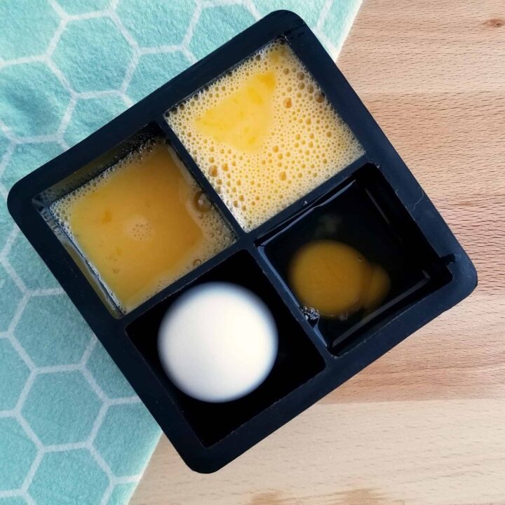Freezing eggs in black ice cube tray on a blue towel on a wooden table.